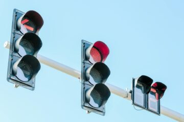 Traffic lights showing red against a clear blue sky on a sunny day. (Photo by Suki Lee on Pexels)