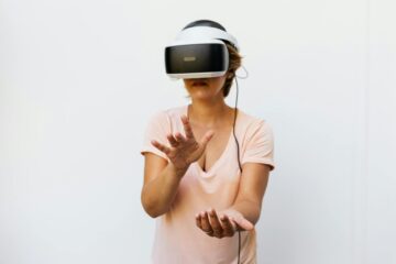 An adult woman interacting with virtual reality using VR goggles, gesturing in excitement. (Photo by www.kaboompics.com on Pexels)