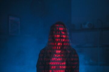 A mysterious silhouette with red binary code projected over the face, set against a dark, moody b... (Photo by cottonbro studio on Pexels)