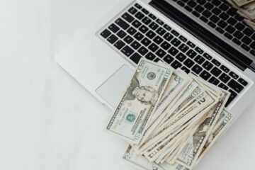 A stack of US dollar bills on a laptop keyboard representing online finance and budgeting. (Photo by www.kaboompics.com on Pexels)