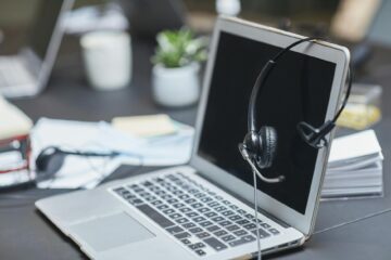 A headset placed on a laptop in a modern, cluttered office setting with papers and plants. (Photo by Jep Gambardella on Pexels)